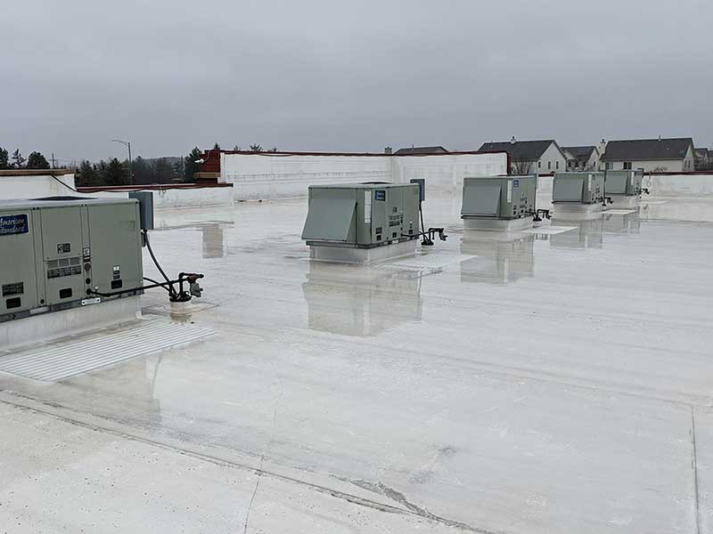 Flat white commercial roof under a stormy sky with AC units lined up in a row